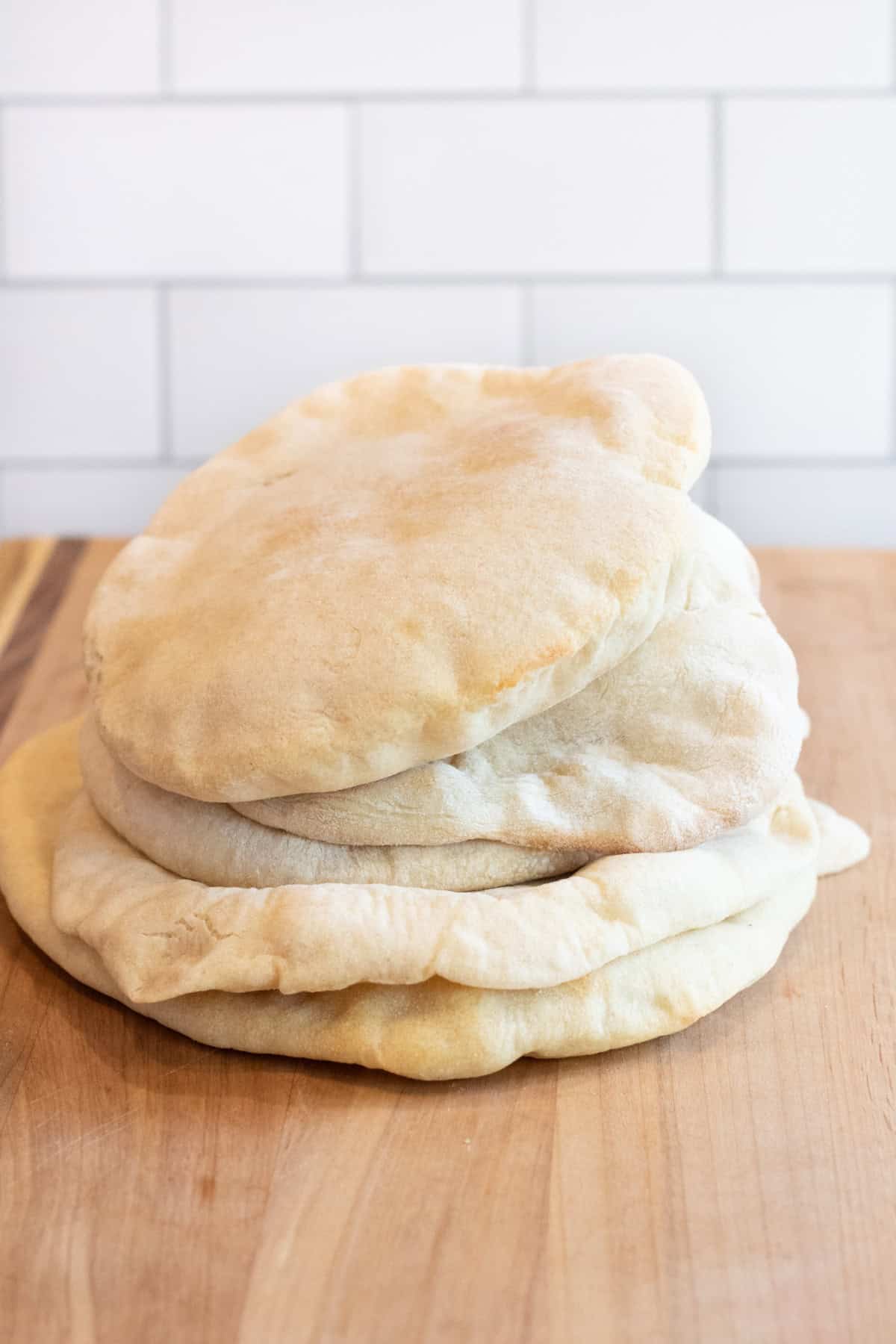 stacked uncut pita breads on a cutting board.