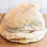 stacked uncut pita breads on a cutting board.