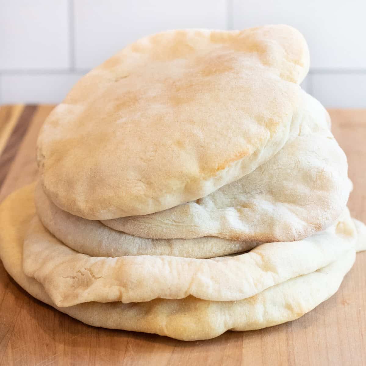 stacked uncut pita breads on a cutting board.