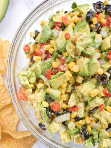 a large bowl of avocado salsa with olive, peppers, and corn.