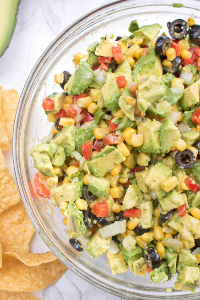 a large bowl of avocado salsa with olive, peppers, and corn.