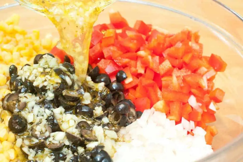 a bowl with olives, red peppers, onion, with dressing being poured in.