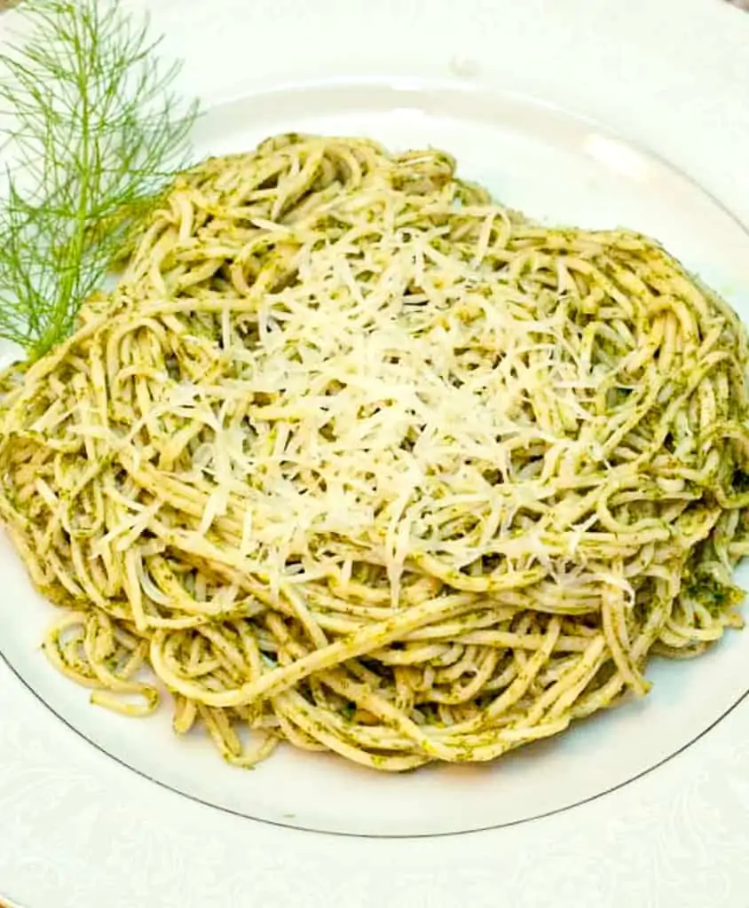 a plate of pesto pasta topped with cheese.