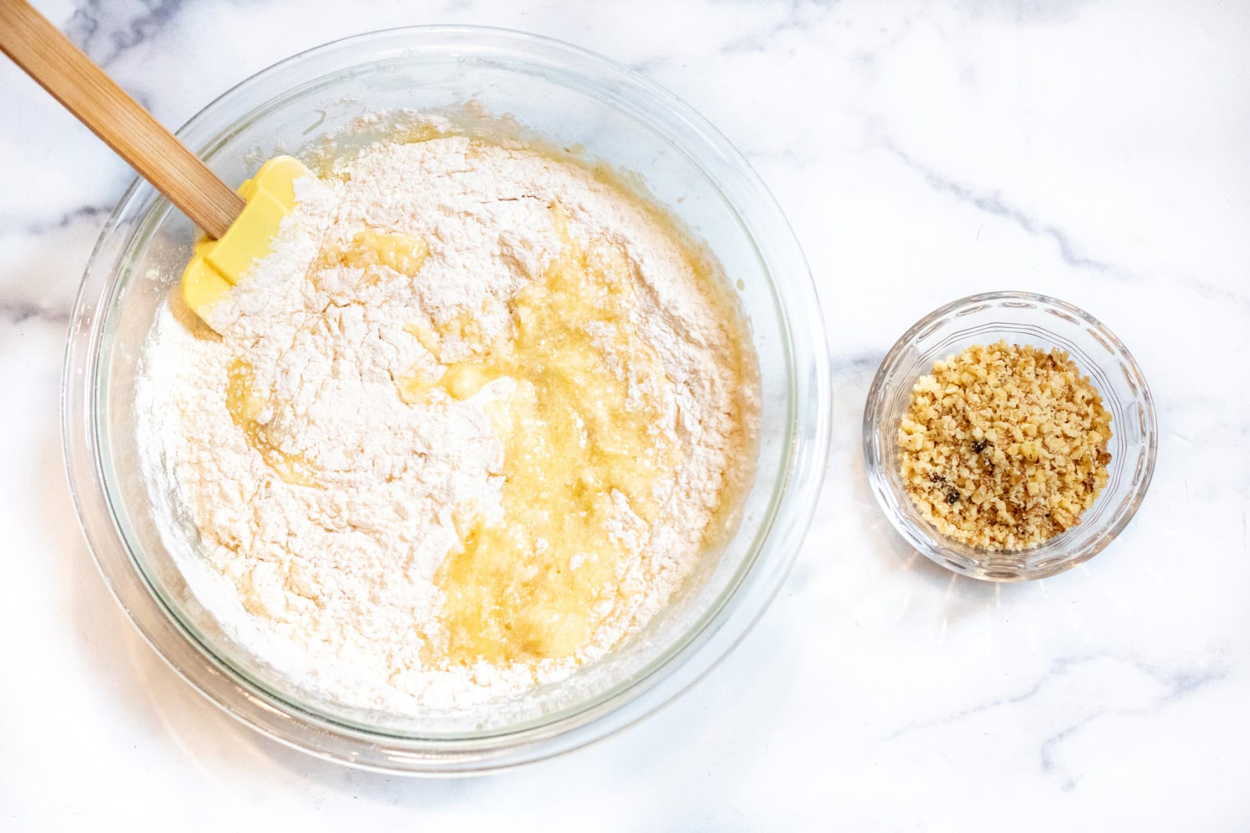 a bowl with flour and egg and banana mixture next to a bowl of chopped walnuts.