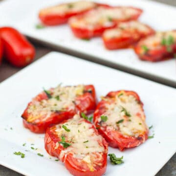 a plate of halved tomatoes with melted cheese on a plate.