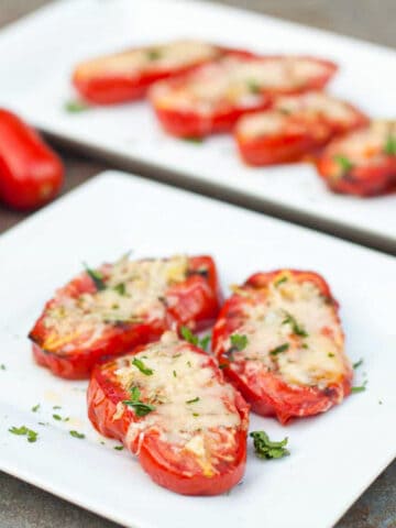 a plate of halved tomatoes with melted cheese on a plate.
