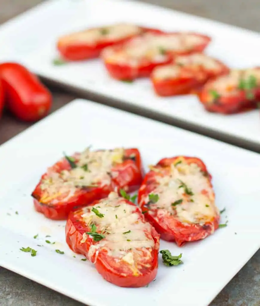 a plate of halved tomatoes with melted cheese on a plate.