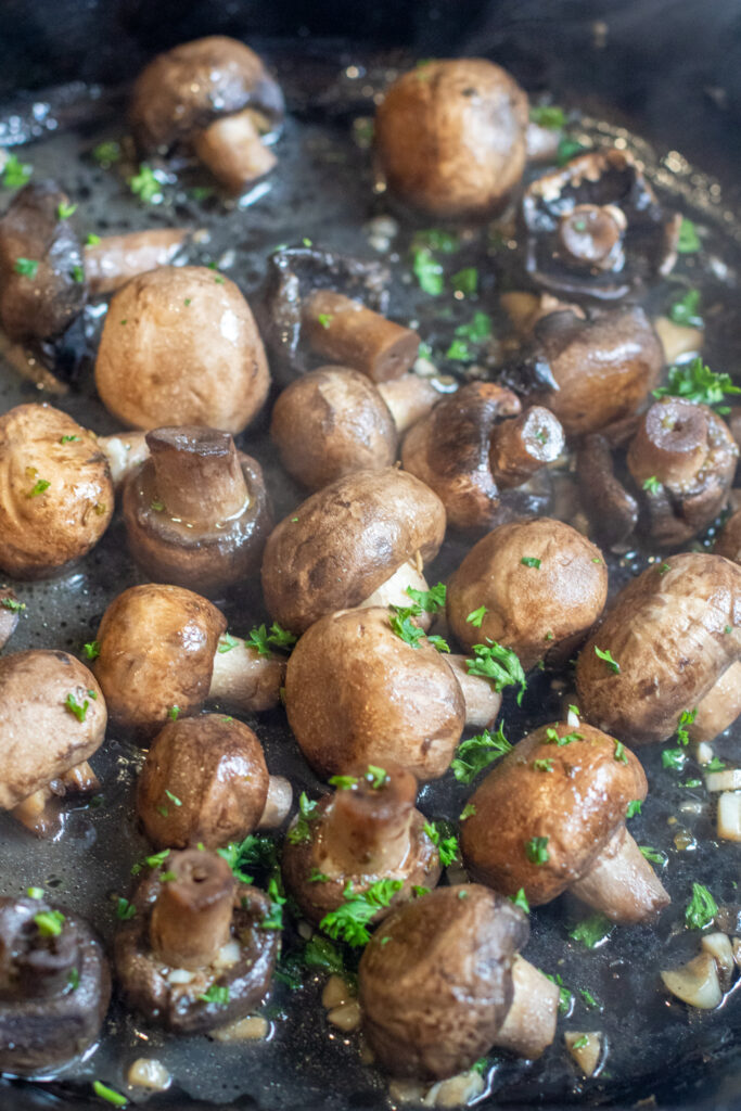 a cast iron with cooked mushrooms in butter and garlc.