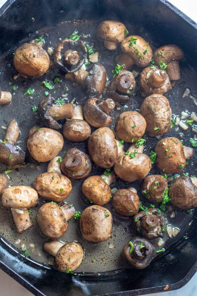 a cast iron with cooked mushrooms in butter and garlc.