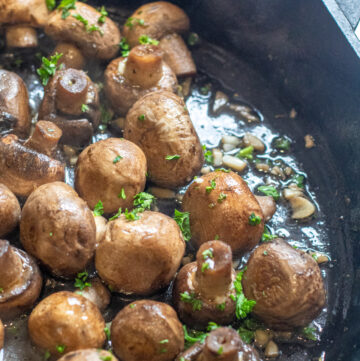 a cast iron with cooked mushrooms in butter and garlc.