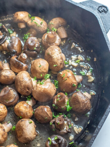 a cast iron with cooked mushrooms in butter and garlc.