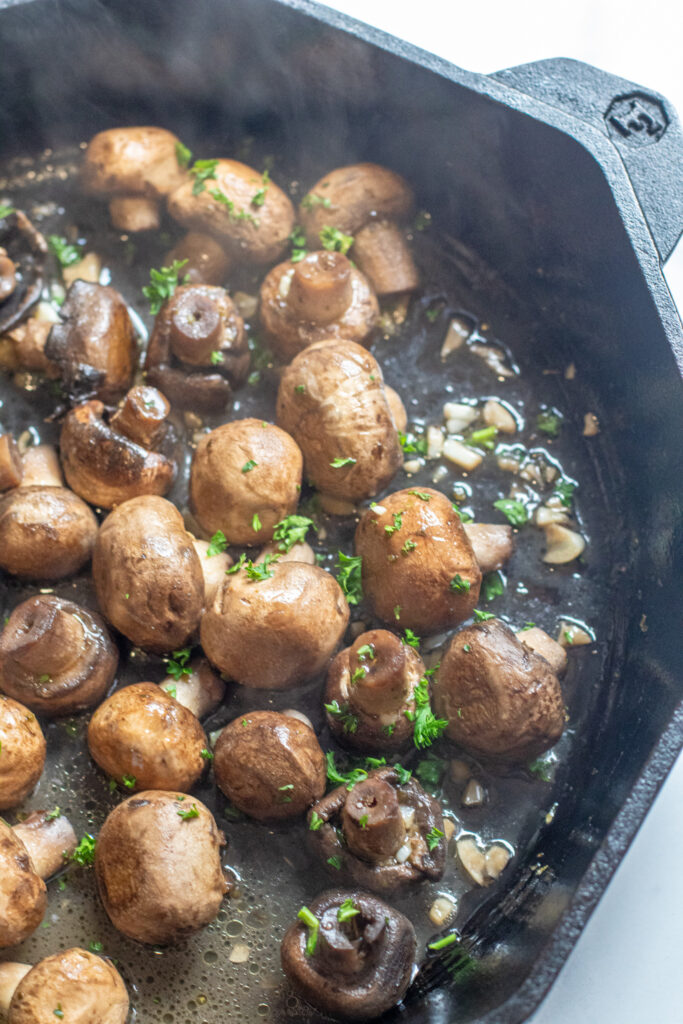 a cast iron with cooked mushrooms in butter and garlc.