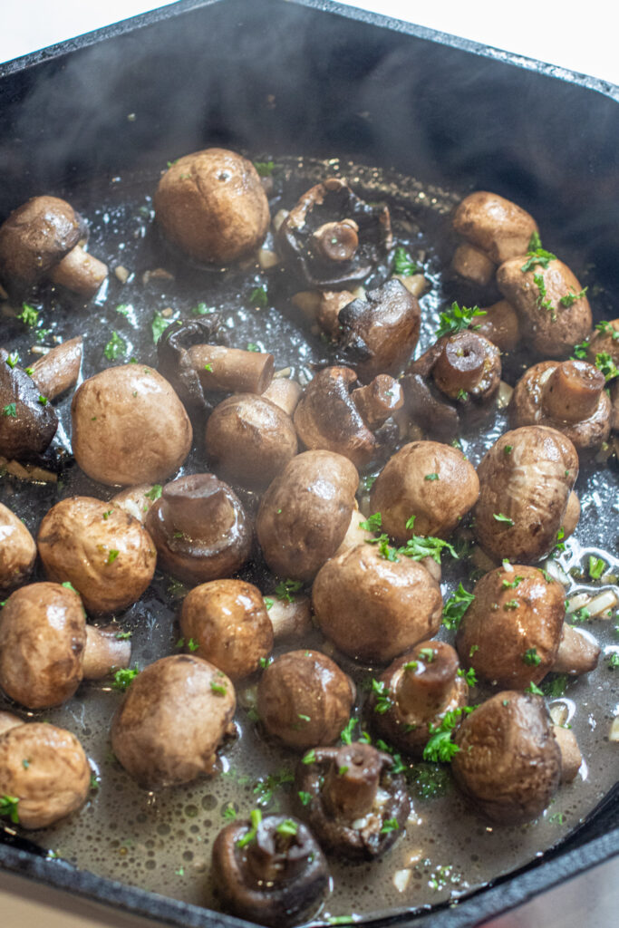 a cast iron with cooked mushrooms in butter and garlc.