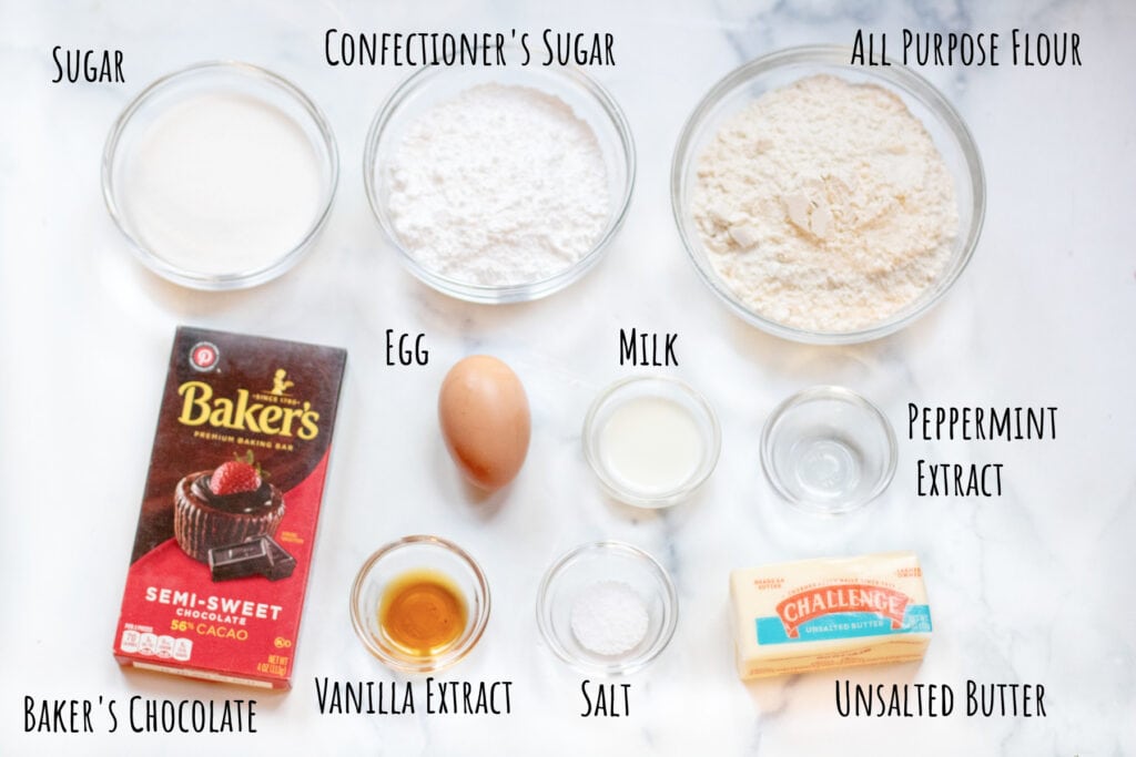 bowls of flour, sugars, a box of bakers chocolate, egg, vanilla extract, butter, peppermint extract, salt, and milk all labeled.