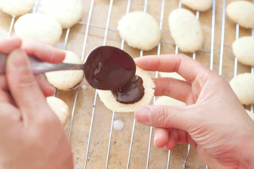 two hands holding cookie and chocolate spooning onto cookie