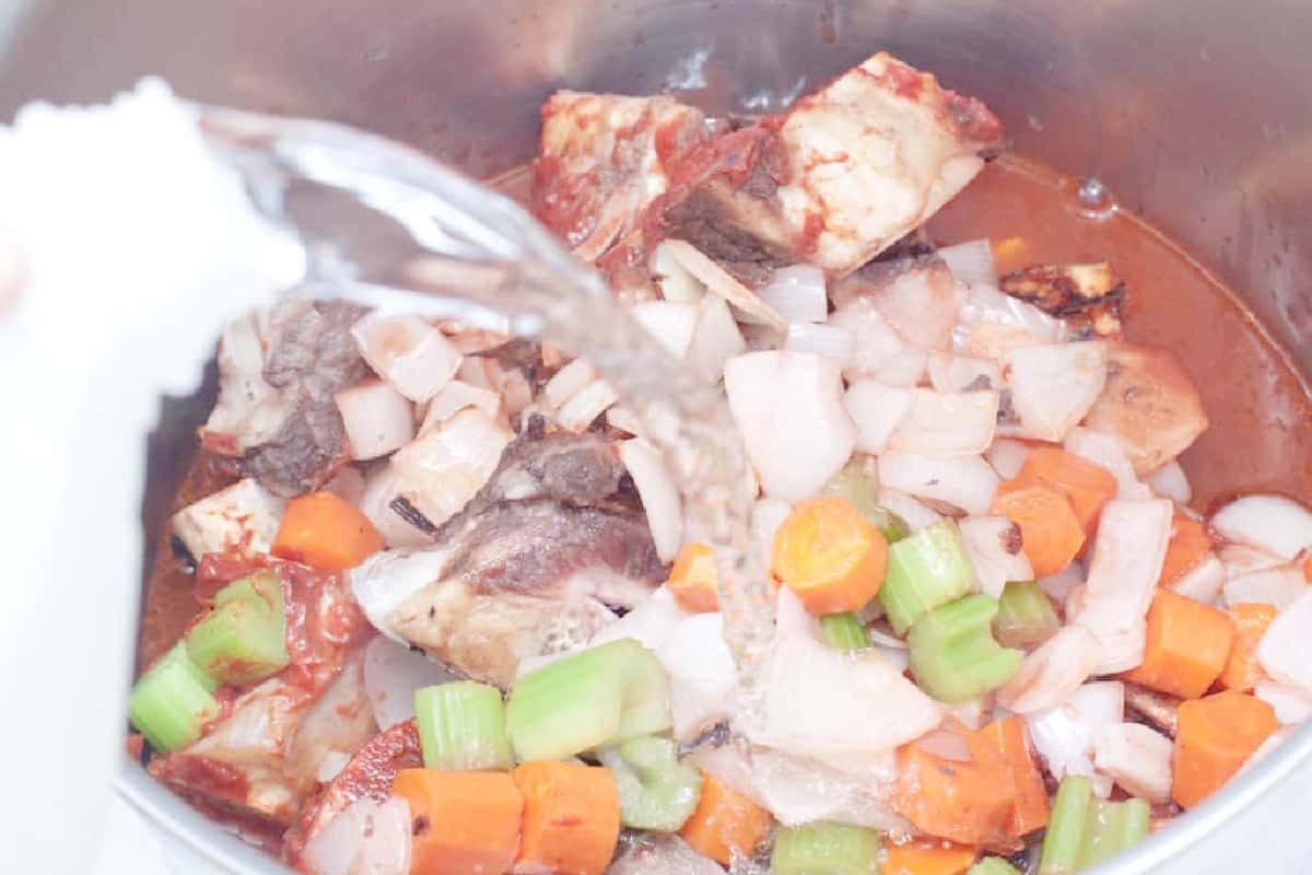 water being poured over veggies, beef bones, in a pot.