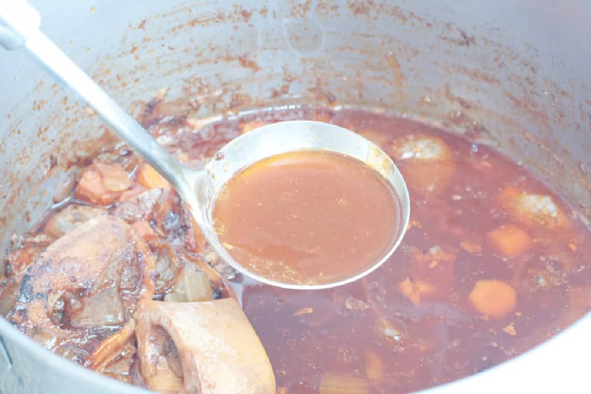 a ladle of beef stock over a pot.