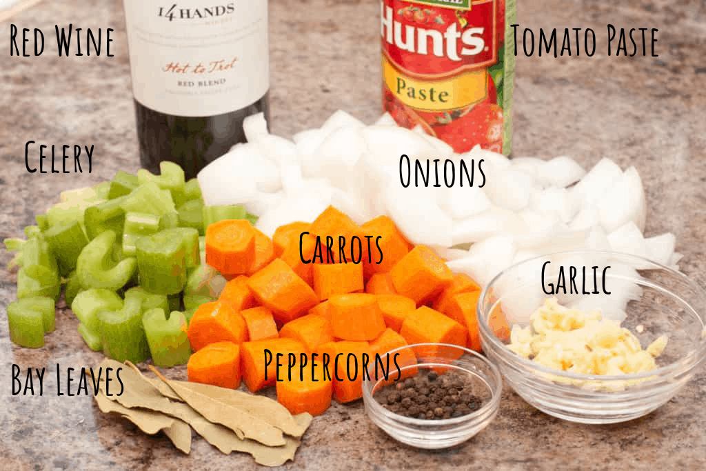 diced carrot, celery, onion on counter with bay leaves, peppercorns, tomato paste, garlic, and bottle of red wine