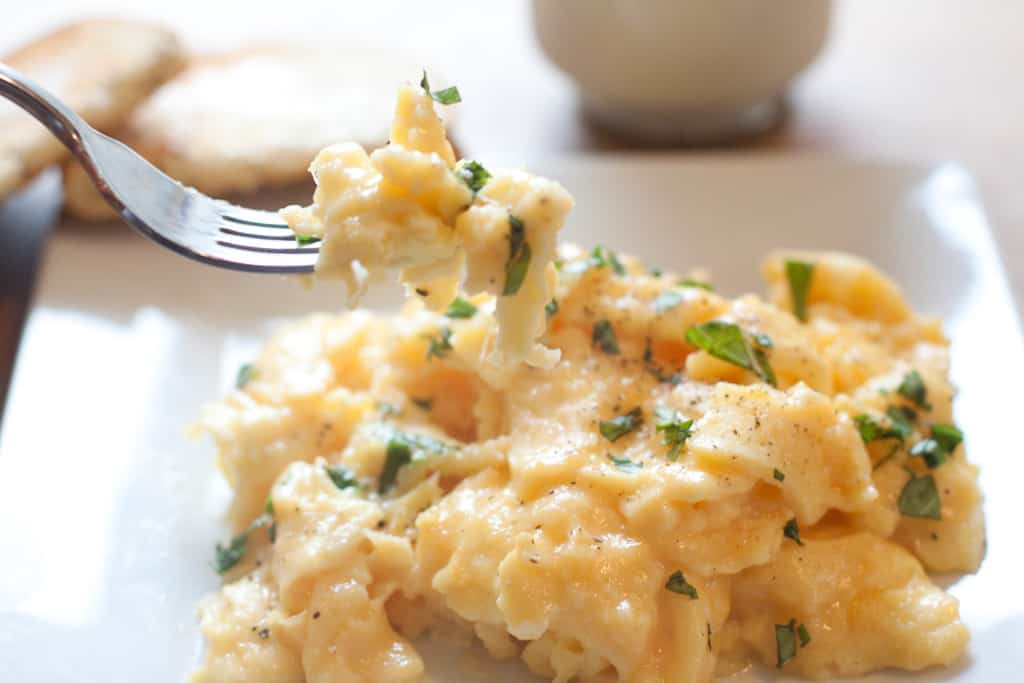 a plate of soft scrambled eggs with fresh basil and a fork holding up a bite. 