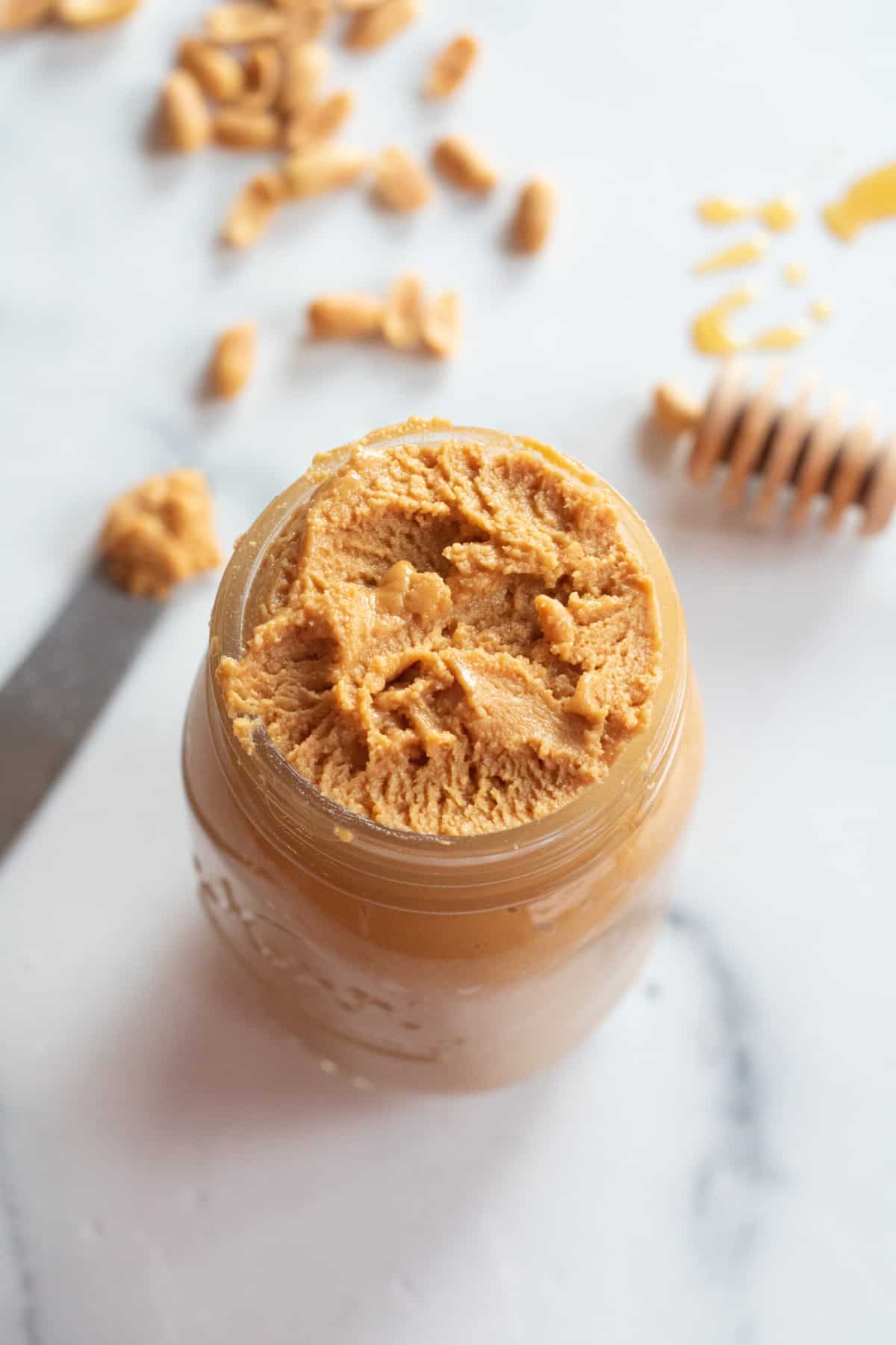 an overhead of an open jar of peanut butter with a knife next to it.