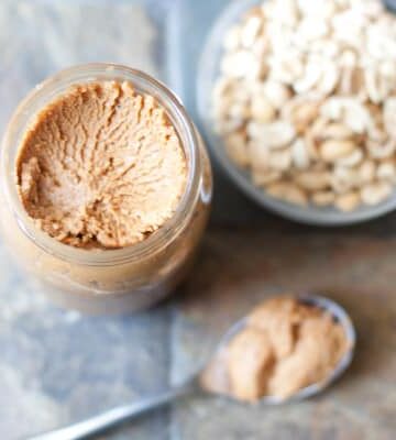 open jar peanut butter with spoon and peanuts