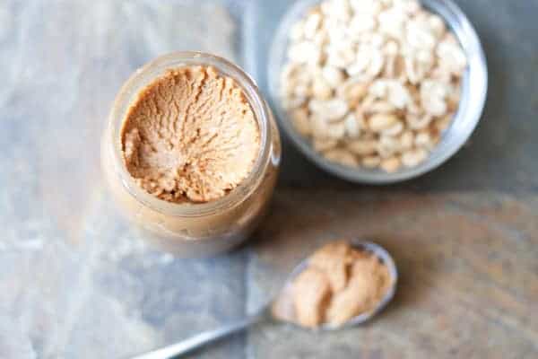 open jar peanut butter with spoon and peanuts