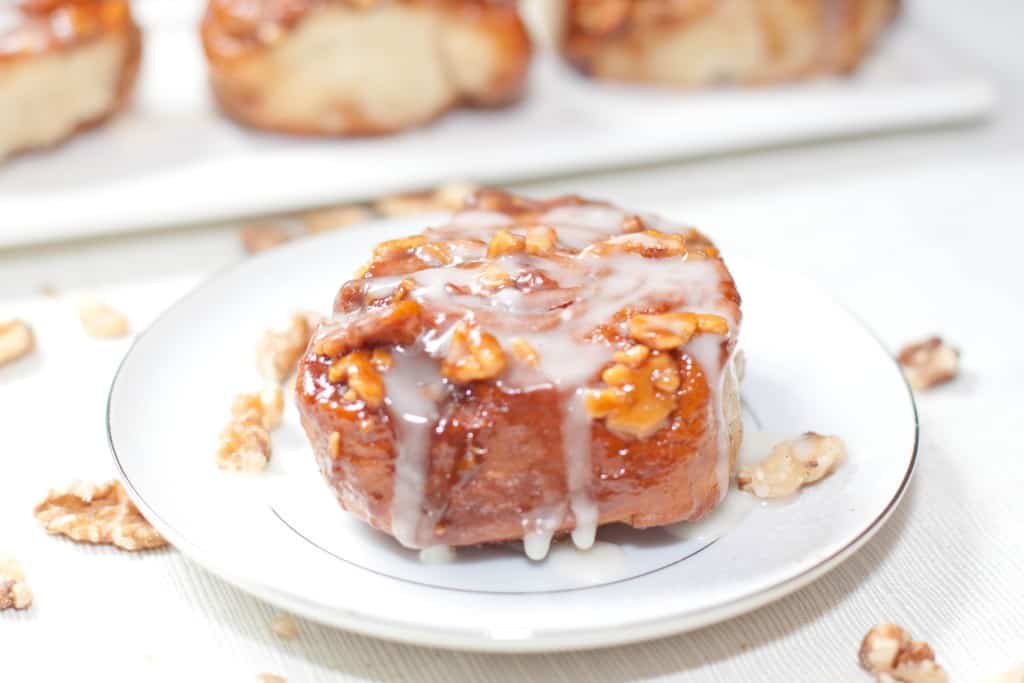 a glazed sticky cinnamon roll with walnuts on a plate.