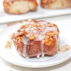 a glazed sticky cinnamon roll with walnuts on a plate.