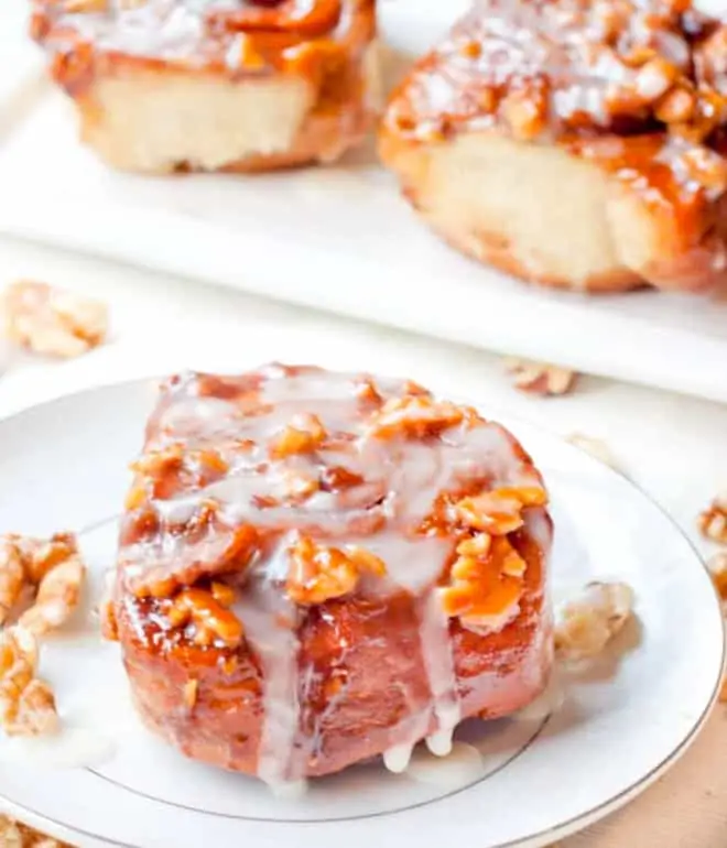 a cinnamon roll with icing and walnuts on a plate.