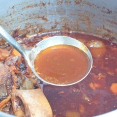 a ladle of beef stock over a pot