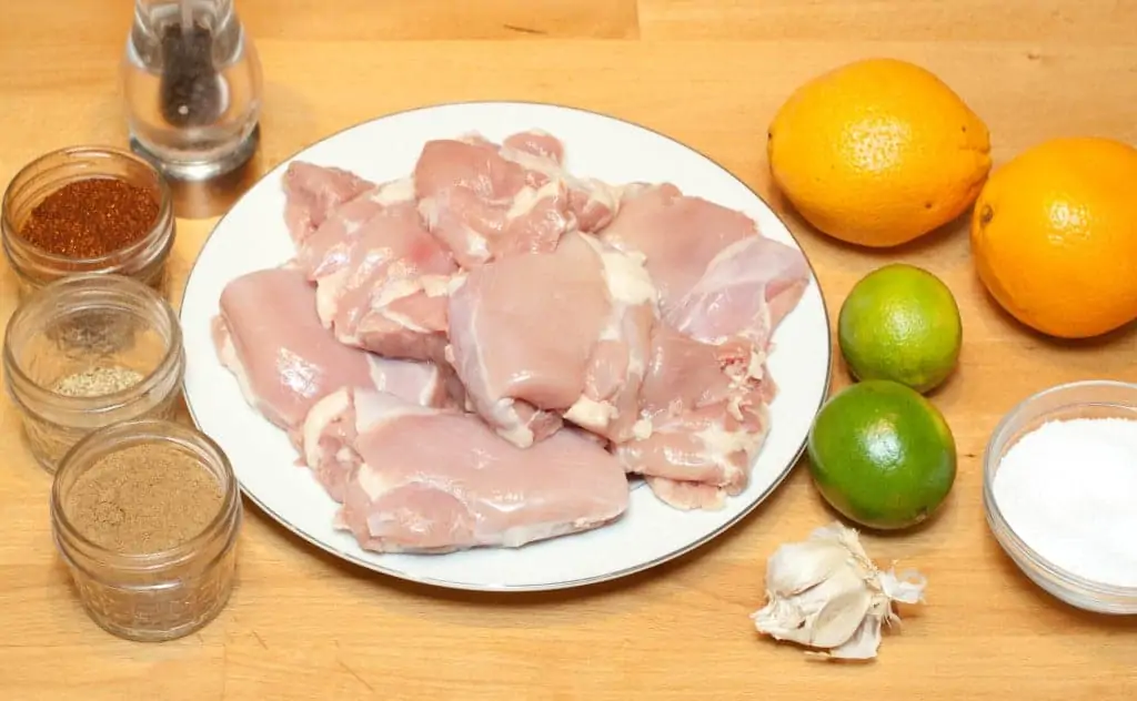 a plate of raw chicken thighs, spices, oranges, limes, garlic, and salt.