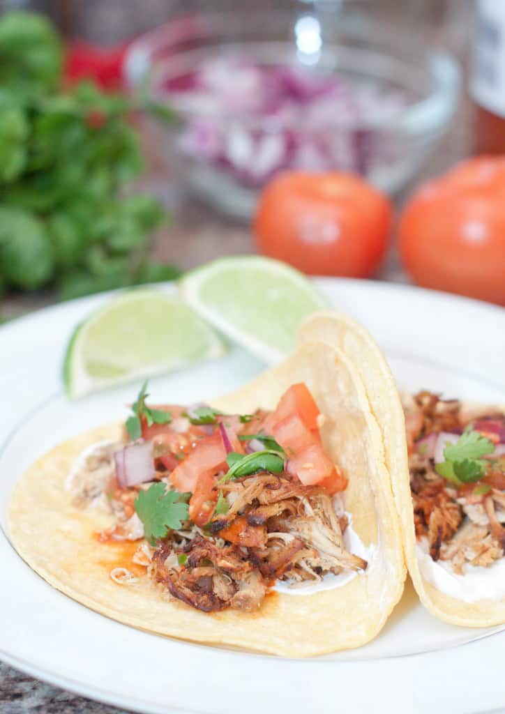 open chicken tacos on plate with tomatoes, onion, and cilantro in background