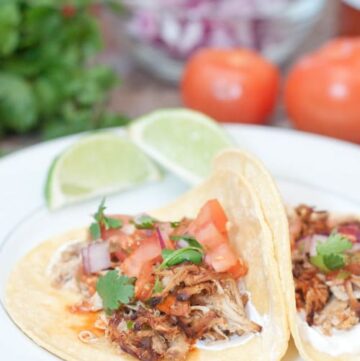 open chicken tacos on plate with tomatoes, onion, and cilantro in background