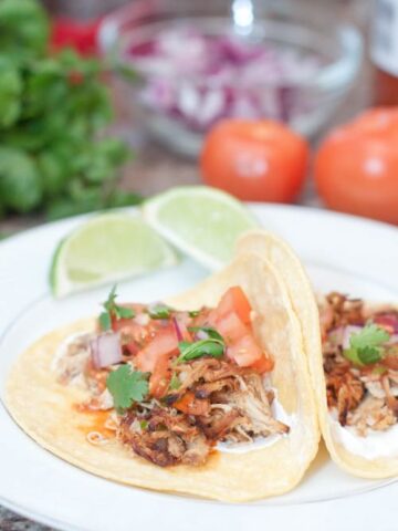 open chicken tacos on plate with tomatoes, onion, and cilantro in background