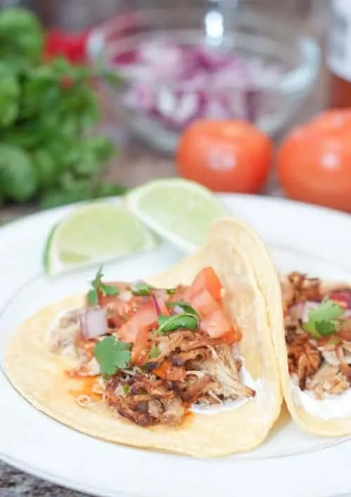 open chicken tacos on plate with tomatoes, onion, and cilantro in background
