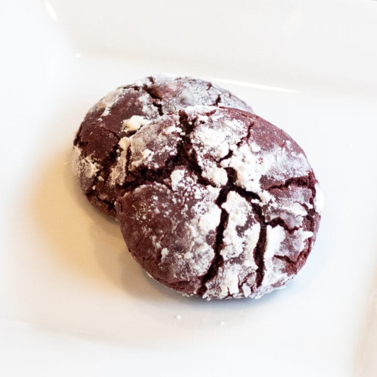 two red velvet cookies coated in powdered sugar on a plate.