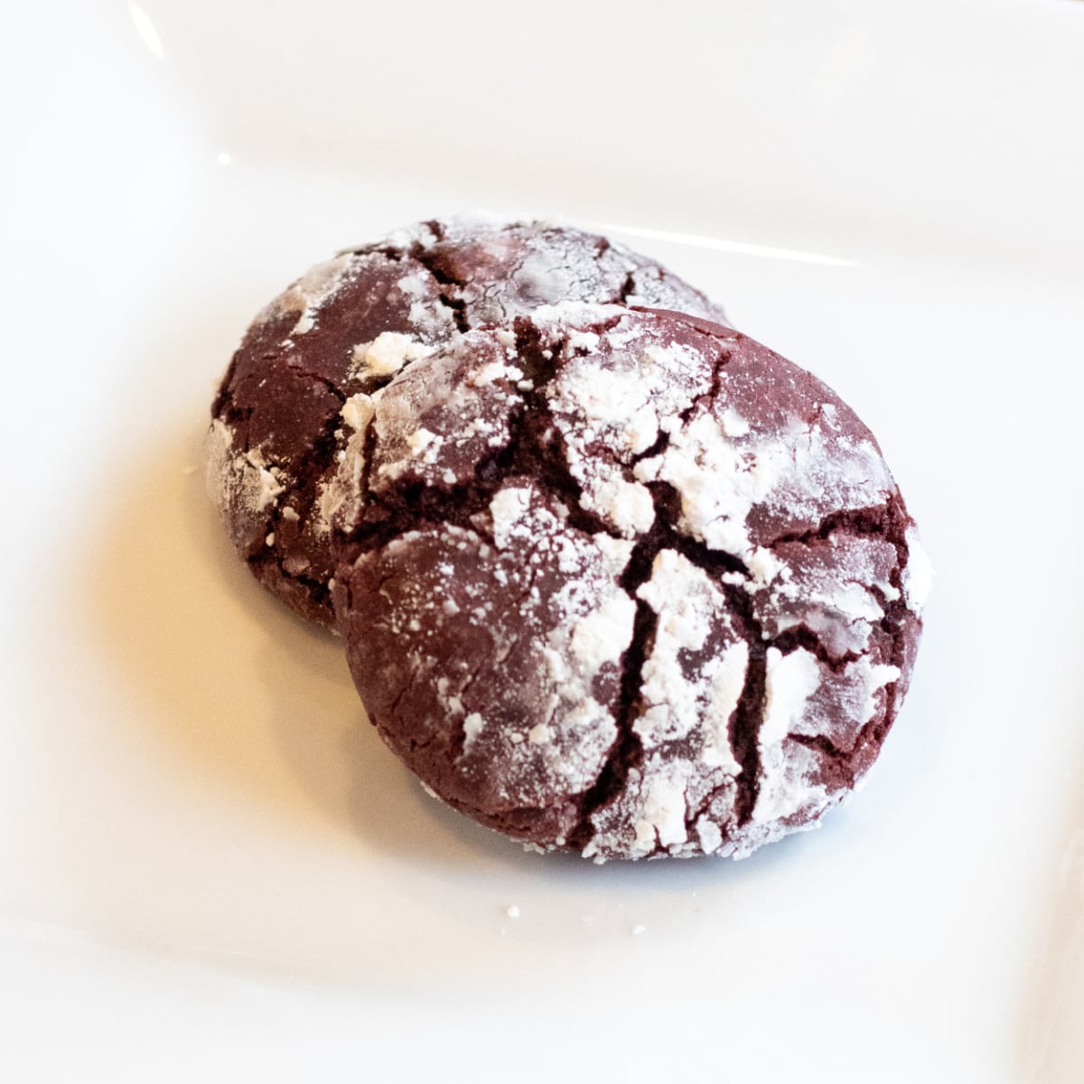 a plate with two red velvet cookies with powdered sugar. 
