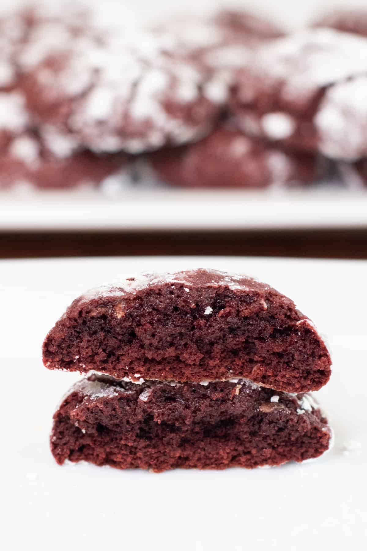 a halved red velvet cookie stacked on a plate in front of another plate of cookies. 