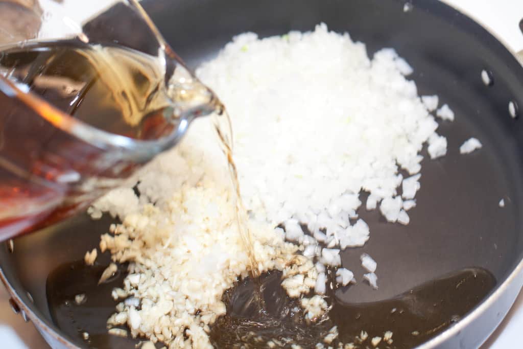 apple cider being poured into a pan with onion