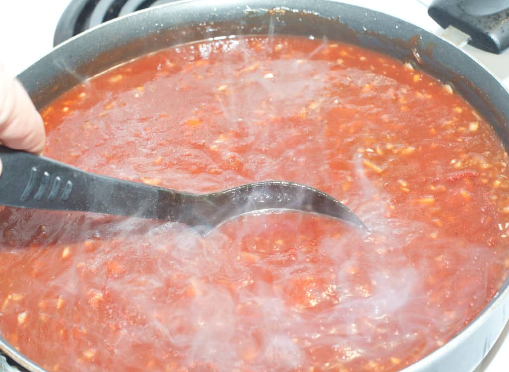 red sauce cooking in a pan with a spoon.