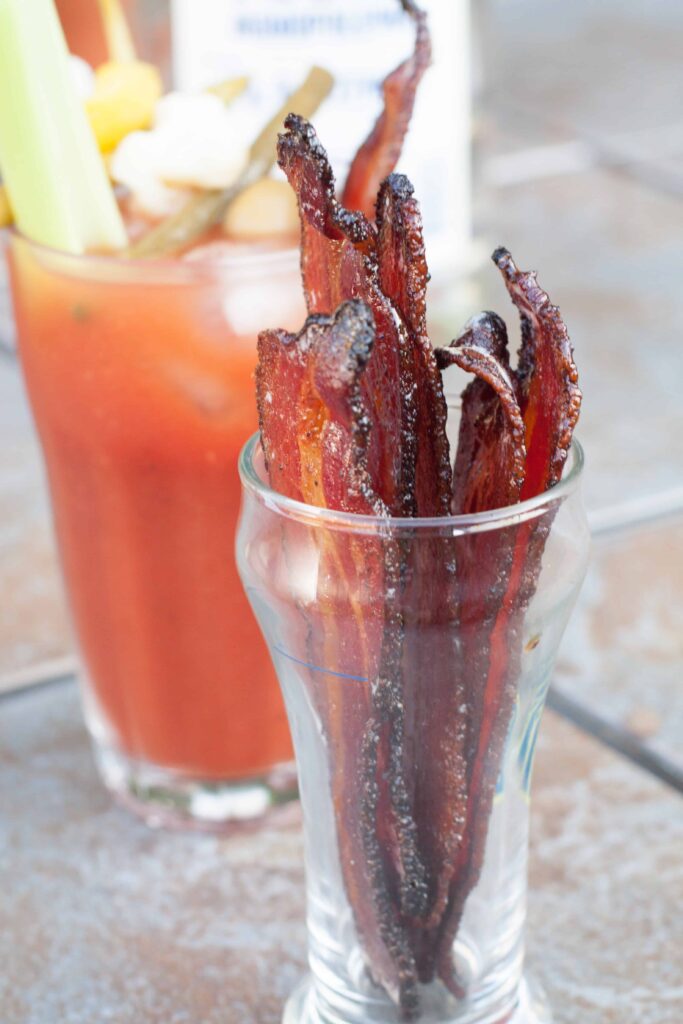 a jar of candied bacon in front of a bloody mary.