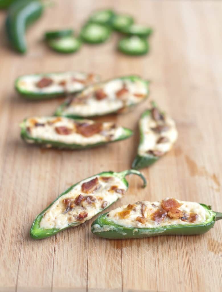 a cutting board with sliced jalapenos stuffed with cheese and topped with bacon.