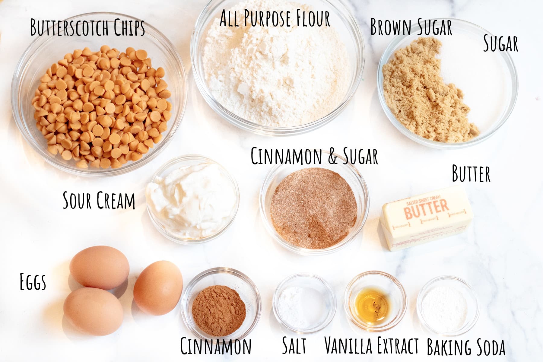 butterscotch chips, flour, sugars, butter, eggs, cinnamon, sour cream, vanilla, cinnamon and sugar, and salt, cream of tarter, and baking soda in bowls.
