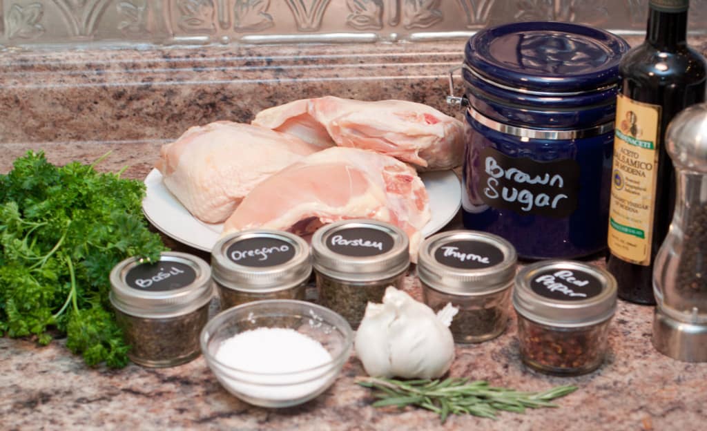 raw chicken breasts, sugar, balsamic, spices, garlic, rosemary, salt, and parsley on counter.