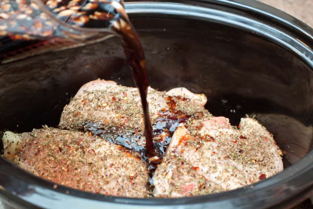 seasoned chicken in a crock pot with balsamic being poured in.