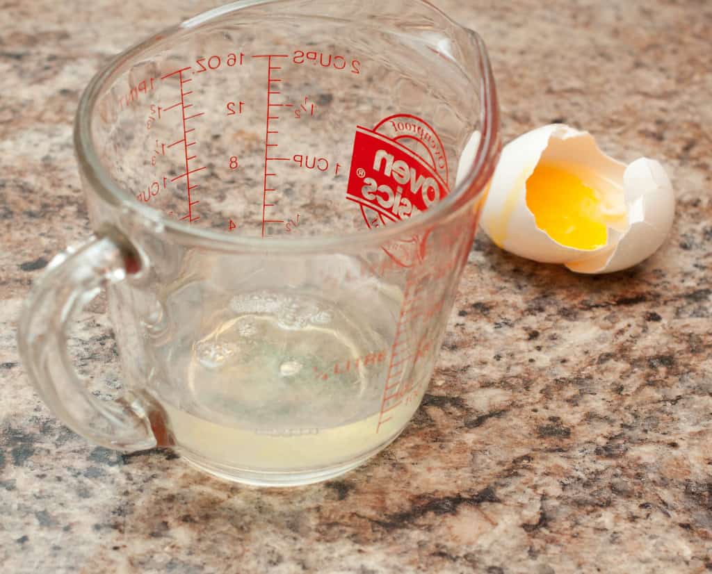 a measuring cup with egg white and a cracked egg and yolk on counter.