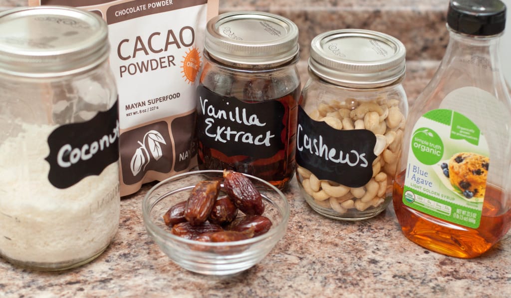 jars of coconut, vanilla extract, cashews, and dates and blue agave, and cacao powder on the counter