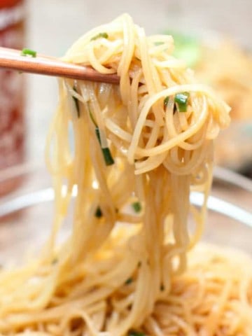 chopsticks holding up noodles with scallions.