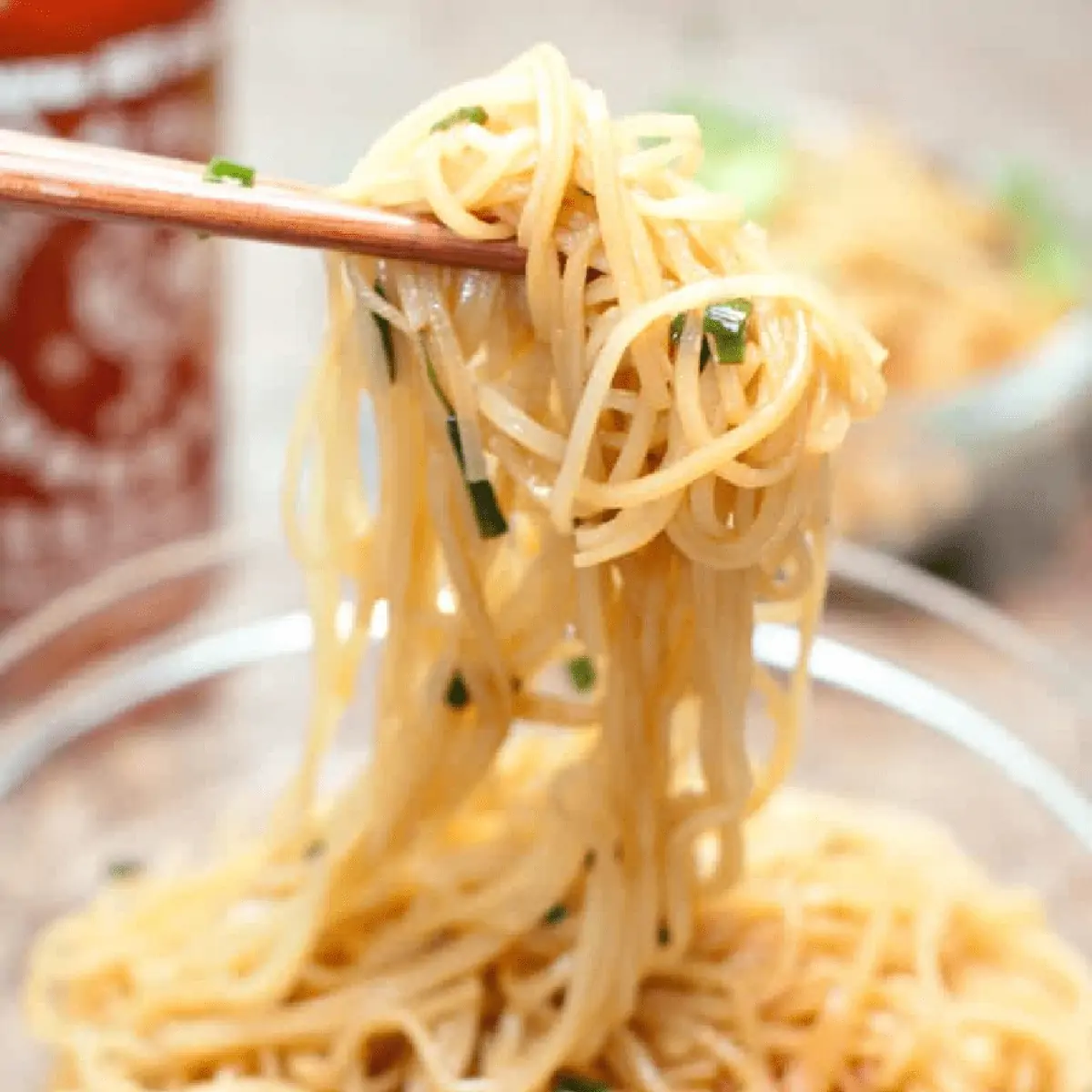 chopsticks holding up noodles with scallions.