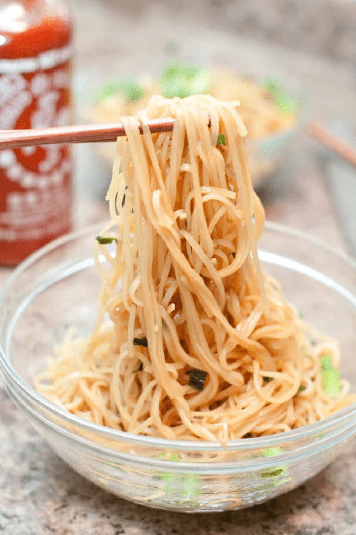 chopsticks holding up noodles with scallions.